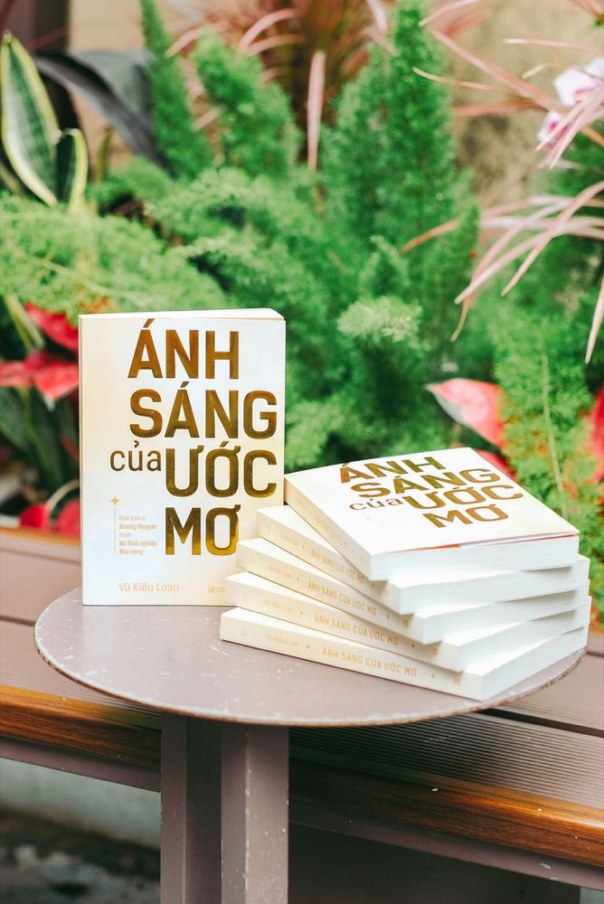 Sách Ánh Sáng Của Ước Mơ trưng bày trên bàn tròn giữa không gian cây xanh