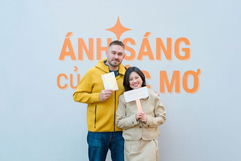 Vũ Kiều Loan cùng khách mời cầm sách trước backdrop lễ ra mắt Ánh Sáng Của Ước Mơ